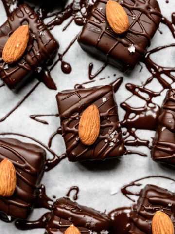Vue rapprochée des barres enrobées de chocolat garnies d'amandes entières et de sel feuilleté sur parchemin.
