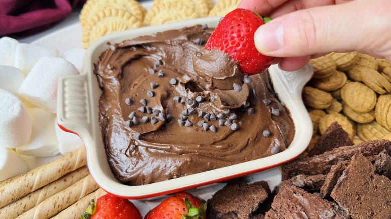Tremper la fraise à la main dans une trempette de pâte à brownie entourée d'autres trempettes