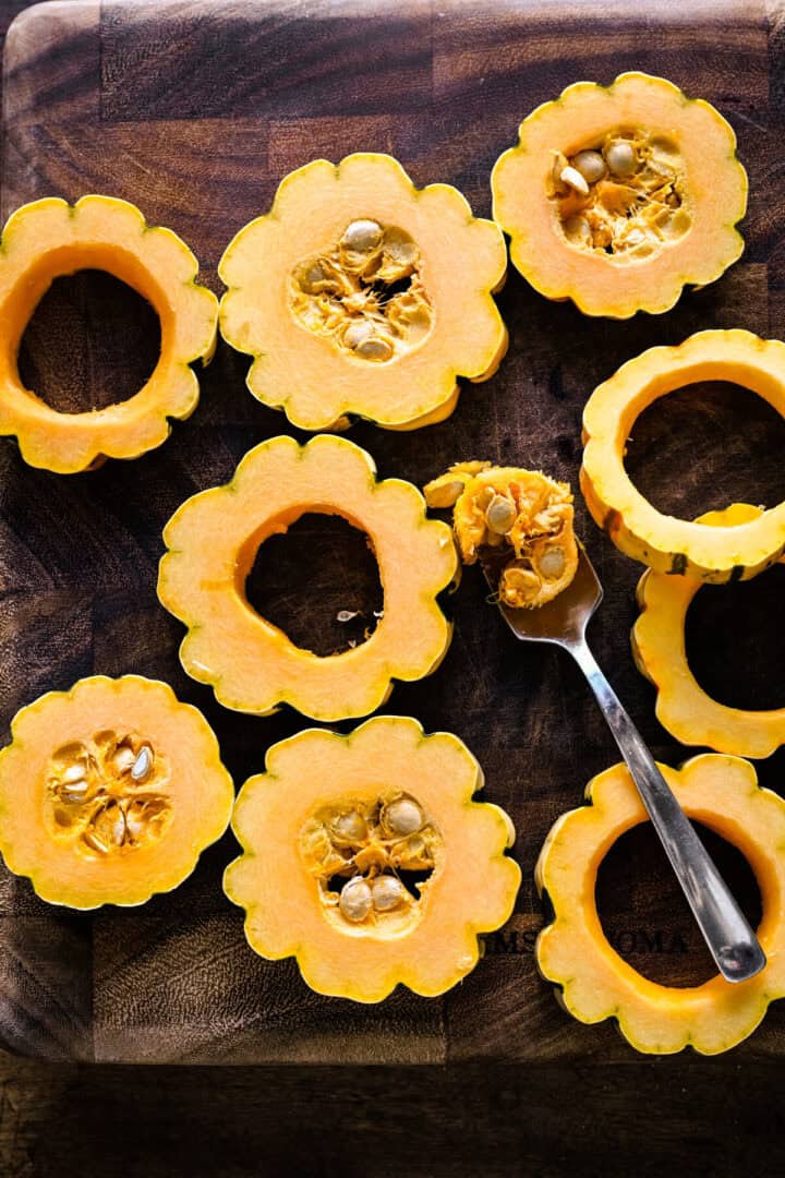 Vue aérienne des rondelles de courge delicata sur une planche de bois, les graines évacuées avec une cuillère.