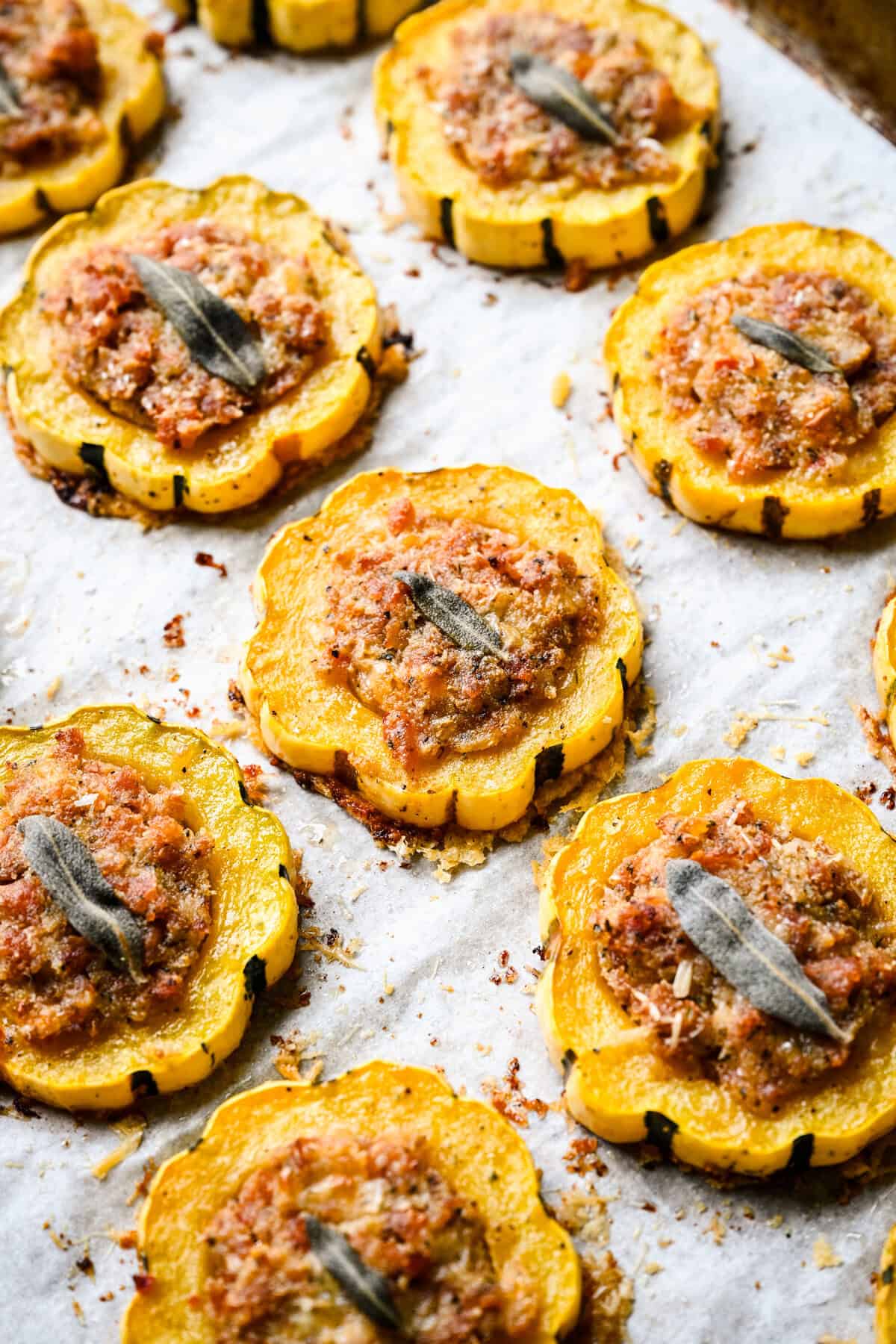 Vue à 45 degrés des anneaux de courge delicata farcis aux saucisses cuites au four sur une poêle tapissée de parchemin.