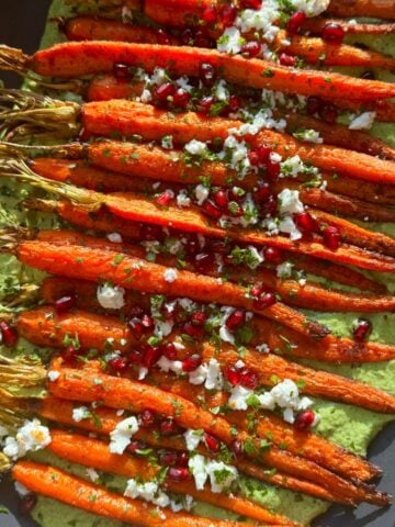Vue aérienne de carottes rôties sur une sauce déesse verte garnie de feta et de grenade.