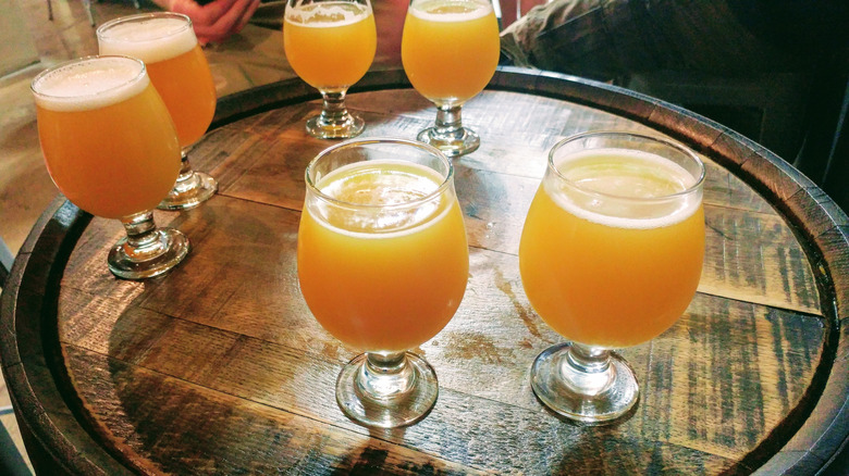Six verres de bière IPA brumeuse de la côte Est sont posés sur un tonneau.