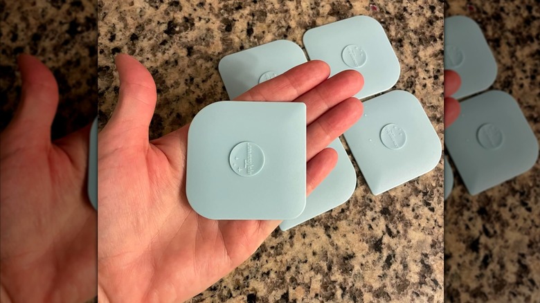 Main d'une personne tenant un grattoir en silicone bleu clair avec quatre autres personnes en arrière-plan sur un comptoir en granit