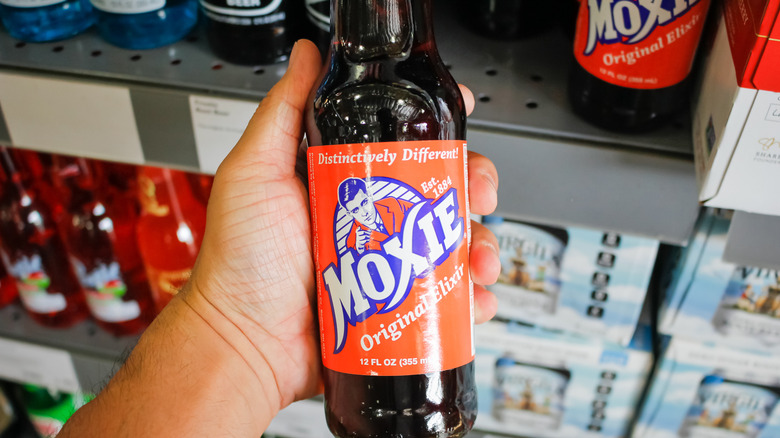 Personne tenant une bouteille de la boisson Moxie Original Elixir