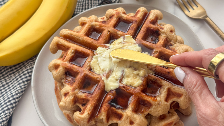 main étalant du beurre sur une gaufre sirupeuse