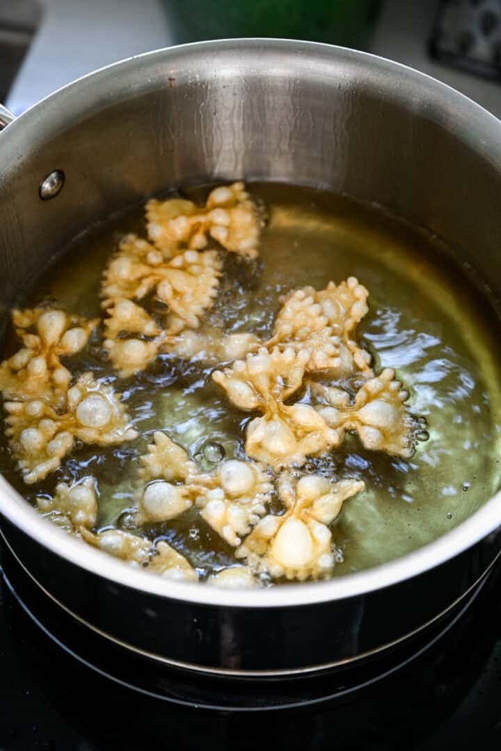 Vue rapprochée des pâtes à nœud papillon gonflées dans de l'huile chaude dans une casserole.