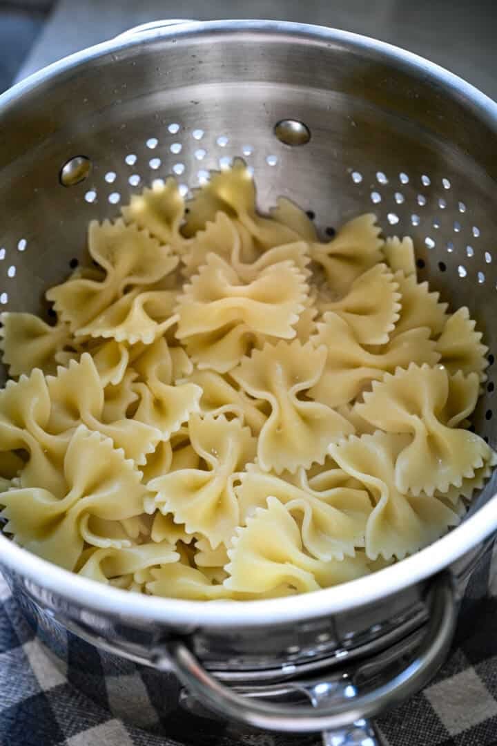 Vue aérienne des pâtes à nœud papillon cuites s'écoulant dans une passoire métallique placée dans une casserole.