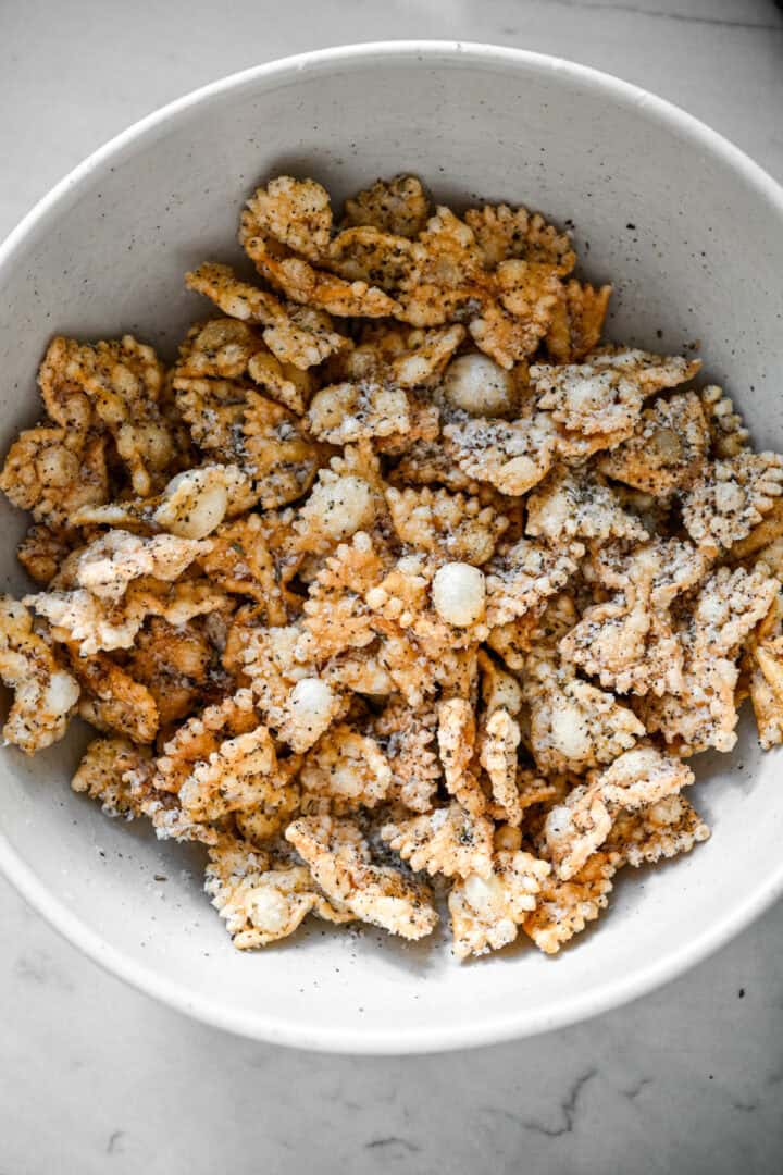 Vue aérienne de pâtes soufflées agrémentées de parmesan râpé et de poivre noir dans un bol blanc.