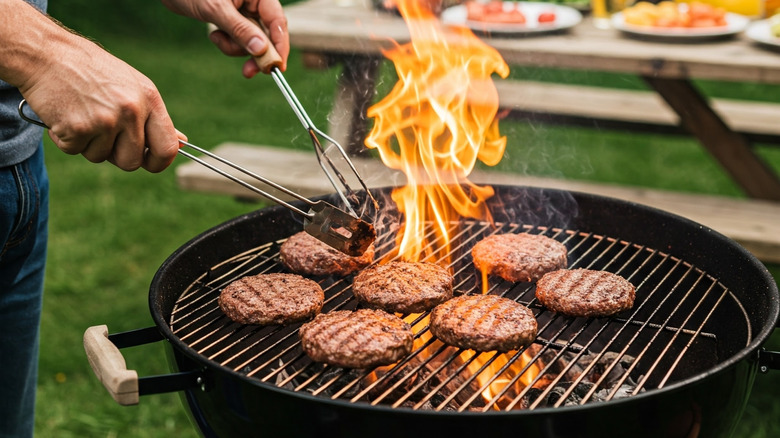Un homme grille des hamburgers sur un gril à charbon de bois.