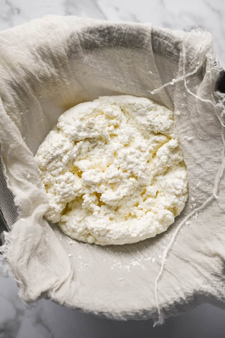 Vue rapprochée du fromage cottage égoutté dans une étamine sur une passoire à mailles fines