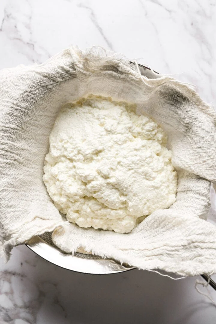 Vue aérienne du fromage cottage frais en grains s'écoulant dans une passoire doublée d'étamine