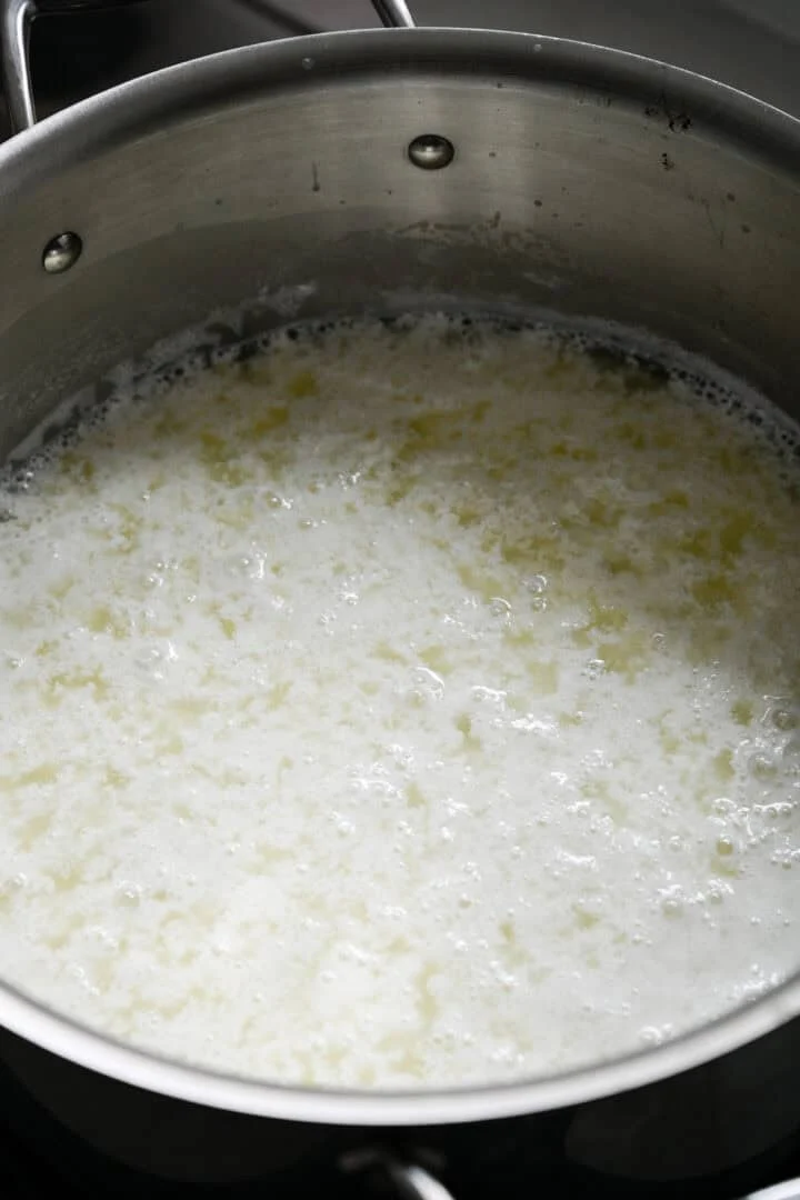 Vue à 45 degrés du lait se séparant en caillé et en lactosérum dans une casserole en acier inoxydable après avoir ajouté du vinaigre