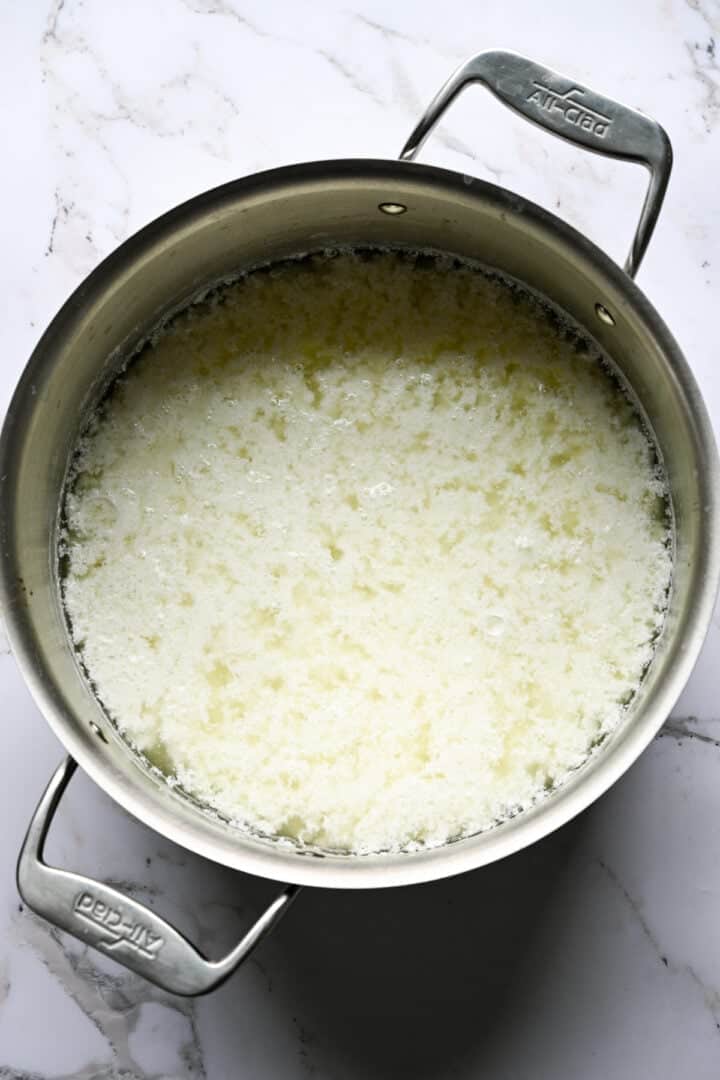Vue aérienne du fromage cottage en grains séparé du lactosérum dans un pot All-Clad sur marbre