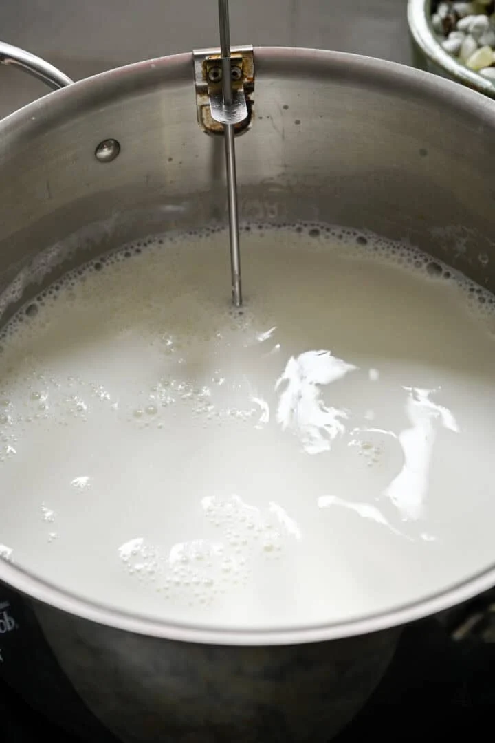 Réchauffer du lait entier dans une grande marmite en inox avec un thermomètre à pince
