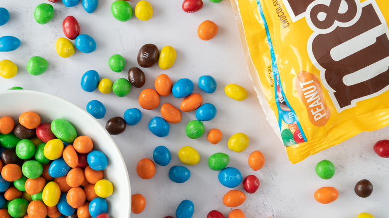 Un sac ouvert de M&Ms aux cacahuètes avec des bonbons dans un bol et dispersés sur une table