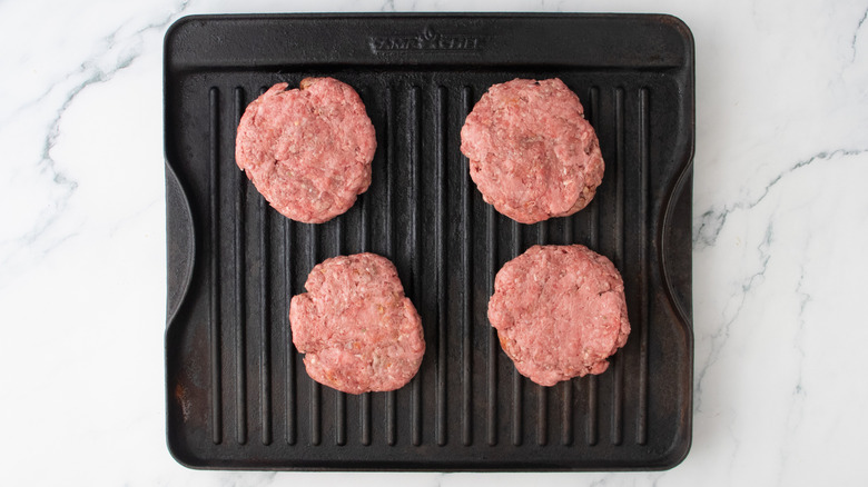 Une grande poêle à griller garnie de quatre galettes de burger