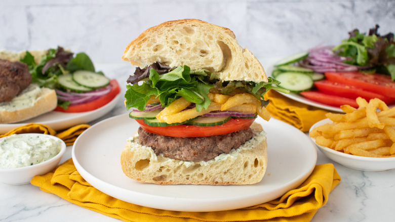 Plan latéral d'un hamburger gyroscopique bien empilé avec garnitures et condiments sur le côté