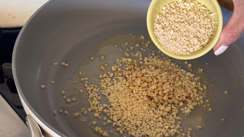 main ajoutant du panko à la poêle avec des pignons de pin