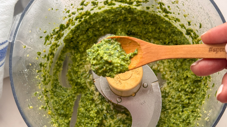 Cuillère de pesto au-dessus du pesto dans un robot culinaire