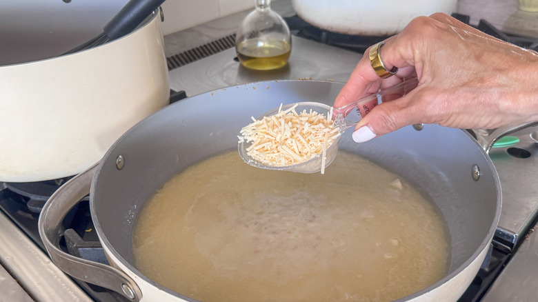 Main tenant une petite cuillerée de parmesan sur une poêle avec une sauce crémeuse