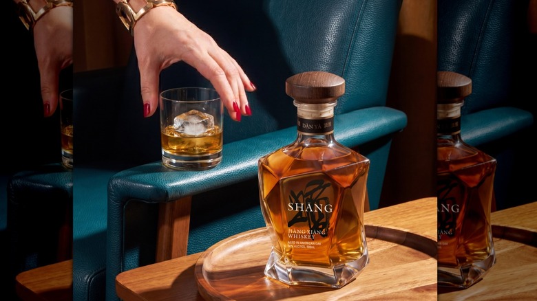 Main cherchant un verre de whisky Shāng avec une bouteille de Dàn Yă au premier plan