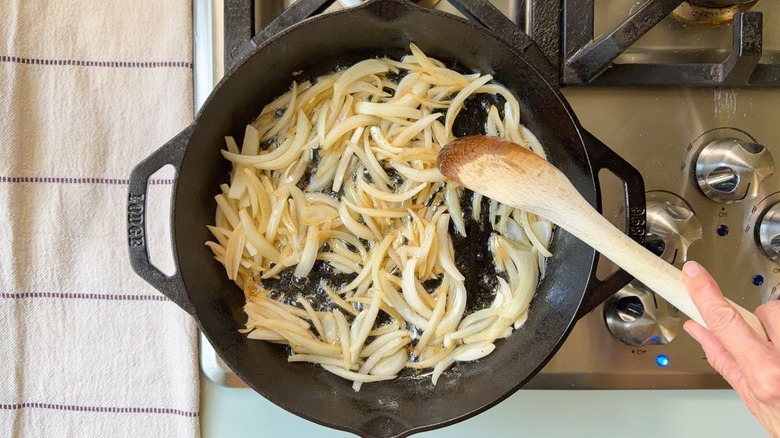 Oignon jaune tranché dans la graisse de bacon dans une poêle sur la cuisinière