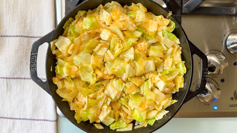 Utiliser des pinces pour remuer le chou cuit dans une poêle sur la cuisinière