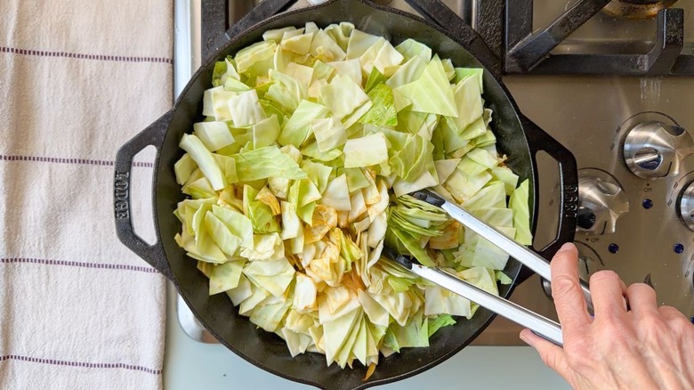 À l'aide de pinces, remuez le chou vert haché dans une poêle sur la cuisinière