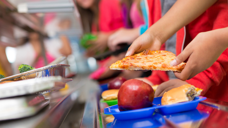Quelqu'un met une part de pizza sur un plateau de repas scolaire