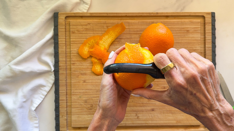 Mains utilisant un éplucheur pour peler une orange