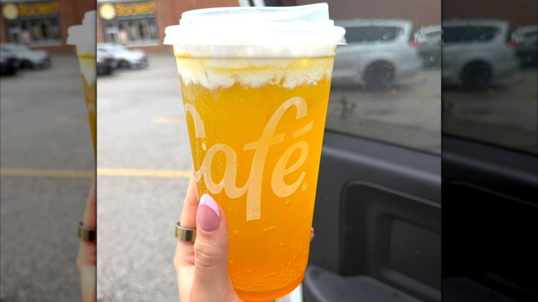 Main d'une personne tenant un Orange Dream avec une boisson Hi-C dans un gobelet en plastique