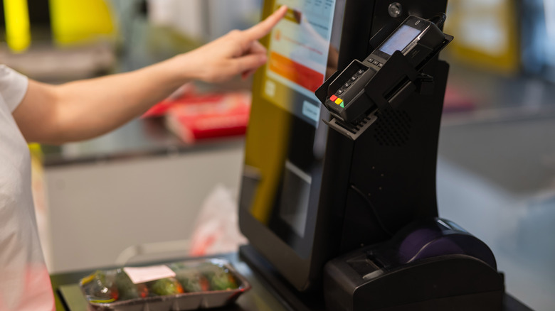 Une personne interagissant avec une borne de paiement automatique pour acheter des concombres