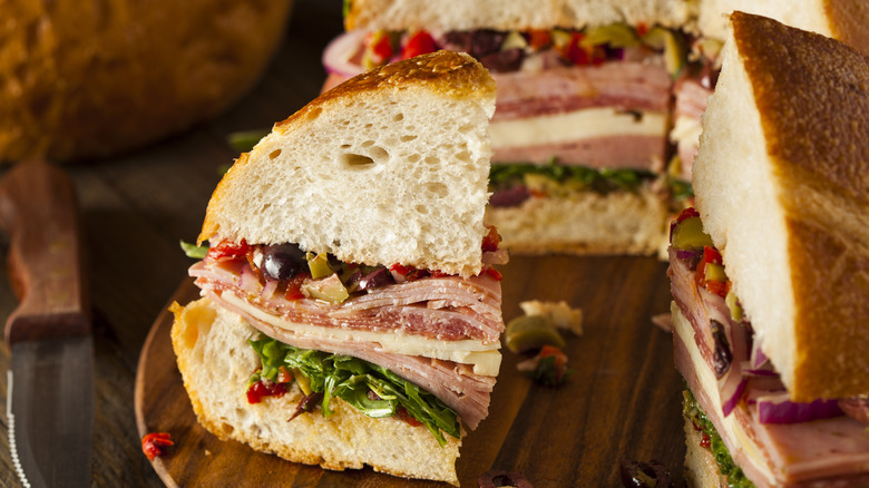 Un sandwich Muffuletta traditionnel coupé en quartiers sur une planche de bois.