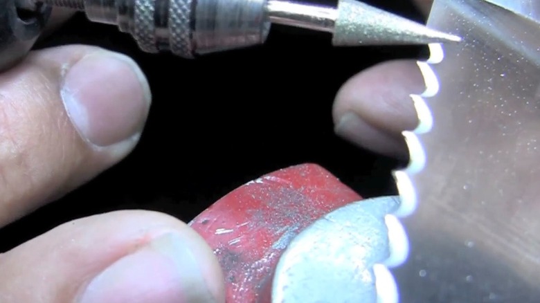 Gros plan d'un foret conique Dremel utilisé sur une lame de couteau dentelée.