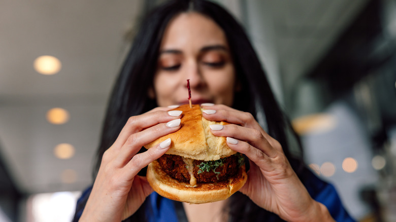 femme dégustant un hamburger empilé.