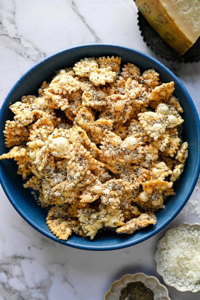 Vue aérienne de pâtes soufflées dans un bol bleu à côté d'un morceau de parmesan et d'un plat de poivre.