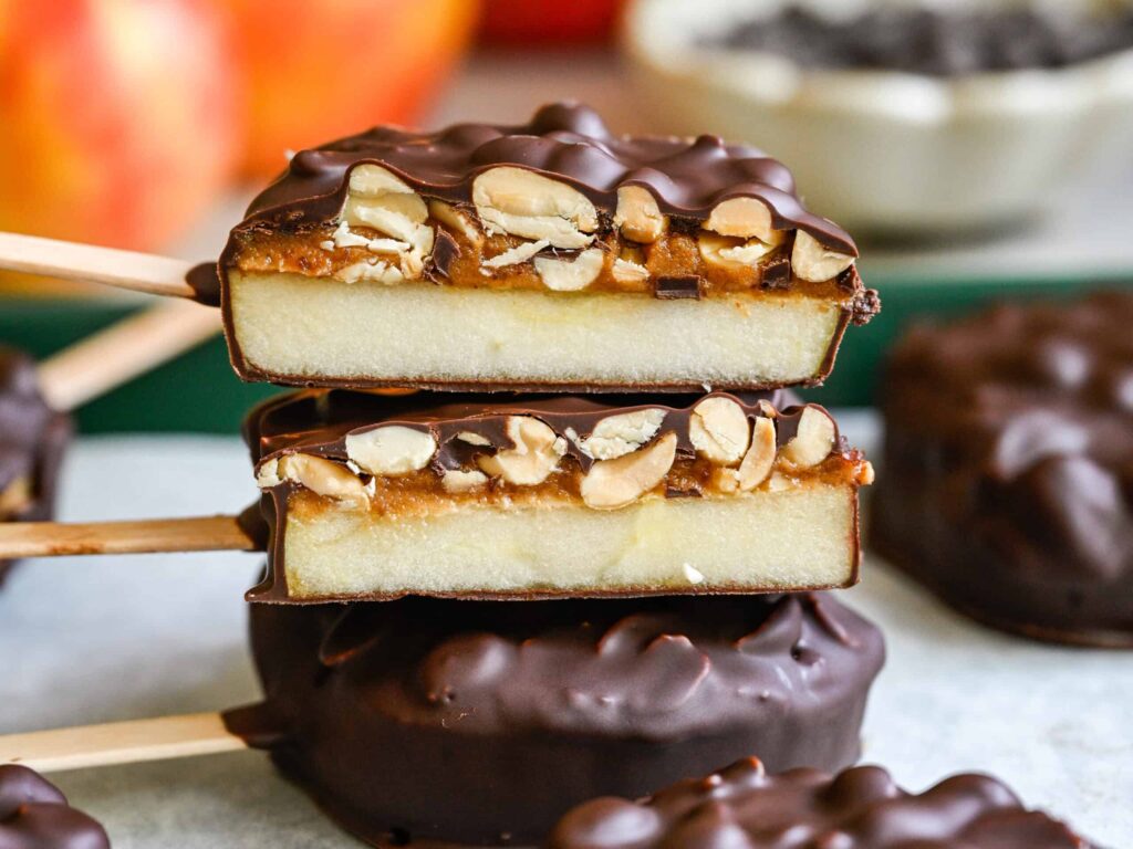 Vue rapprochée de deux tranches de pomme coupées enrobées de chocolat, montrant les couches de pomme, de datte et d'arachide.
