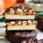 Vue rapprochée de deux tranches de pomme coupées enrobées de chocolat, montrant les couches de pomme, de datte et d'arachide.